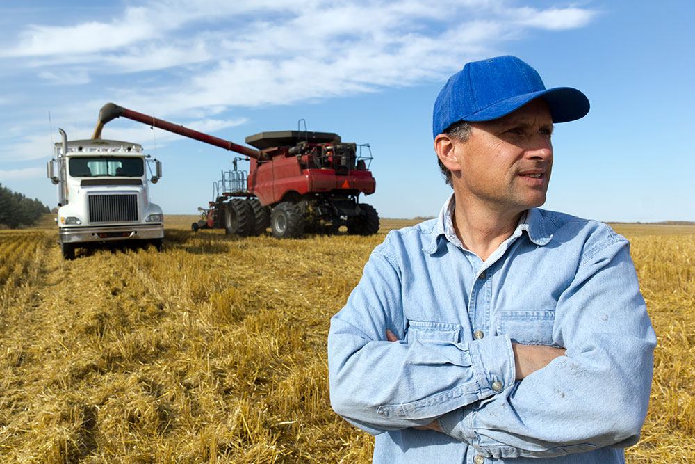 a man in a field with a truck and agricultural equipment behind him